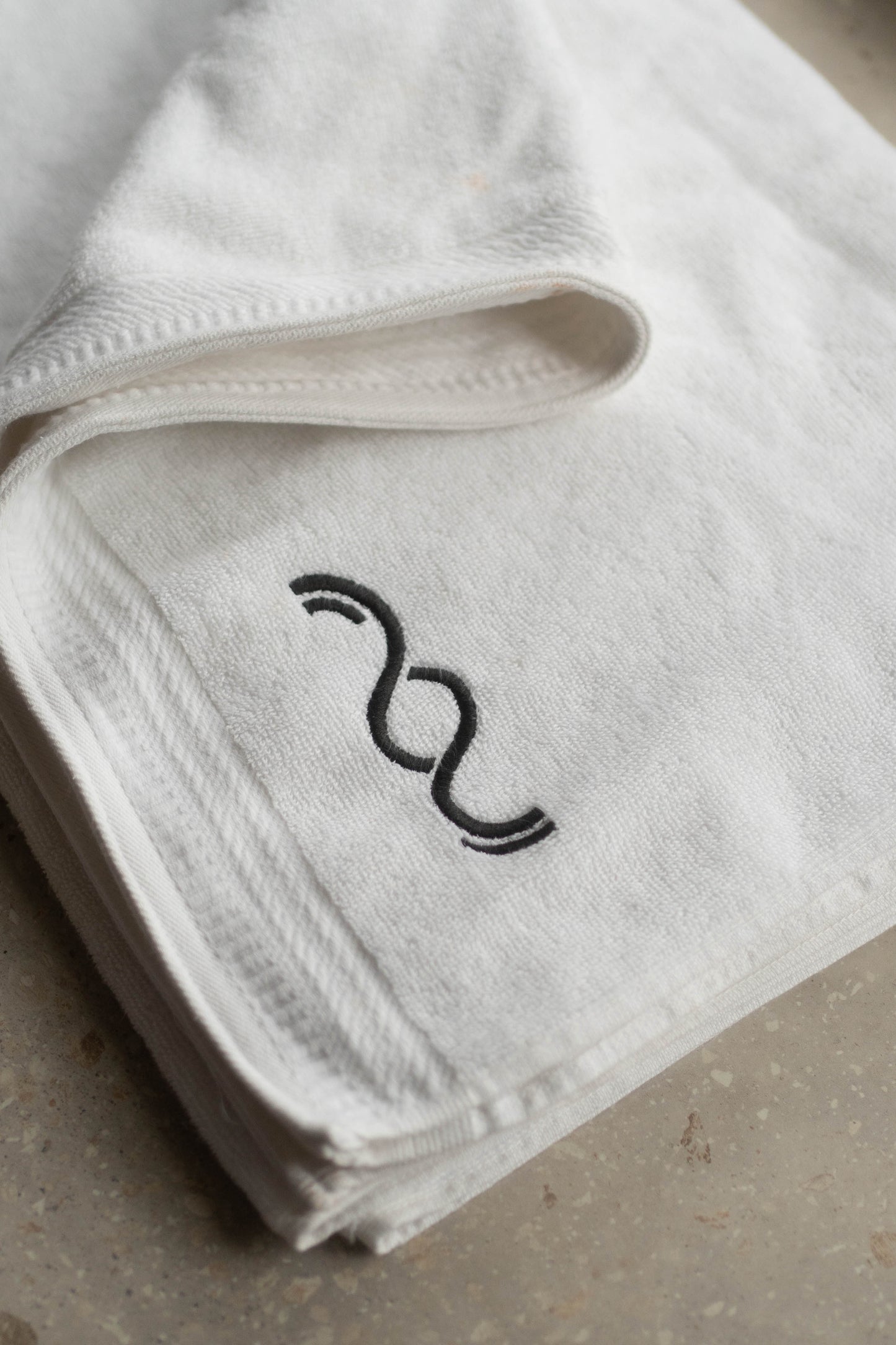 White towel with black embroidered design on a neutral background
